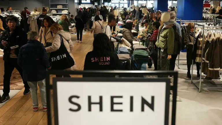 Personas mirando ropa en un local físico de Shein en Europa, con bolsas de la marca colgando de sus hombros