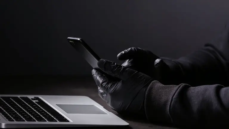 Ladrón con un celular en la mano, hackeando las frases semilla de otro usuario cripto