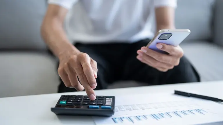 Persona con un celular y una calculadora sacando cuentas de su deuda con una billetera virtual o un banco