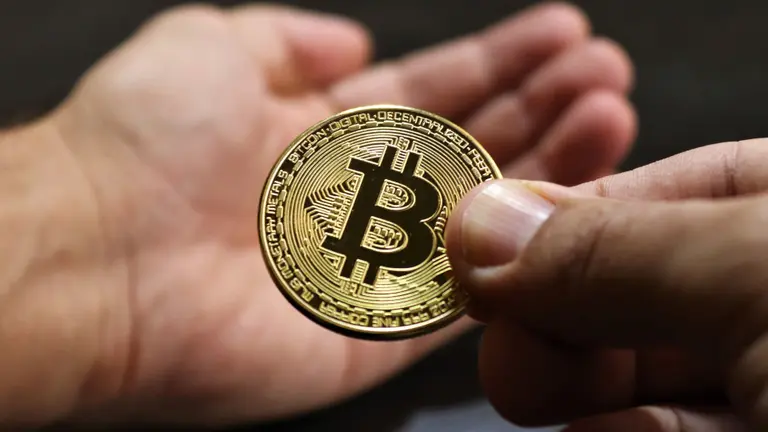 Usuario apoyando en su mano una moneda física de Bitcoin 