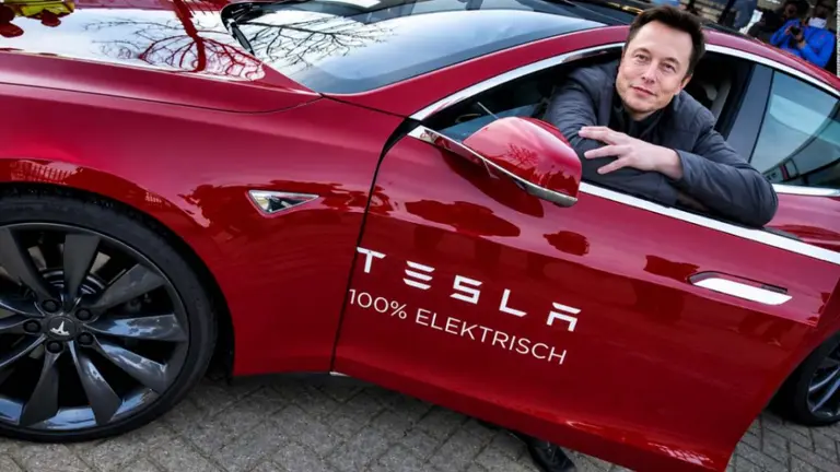 Elon Musk posa dentro de un Tesla rojo, con la puerta abierta, mostrando el interior y el diseño del vehículo eléctrico