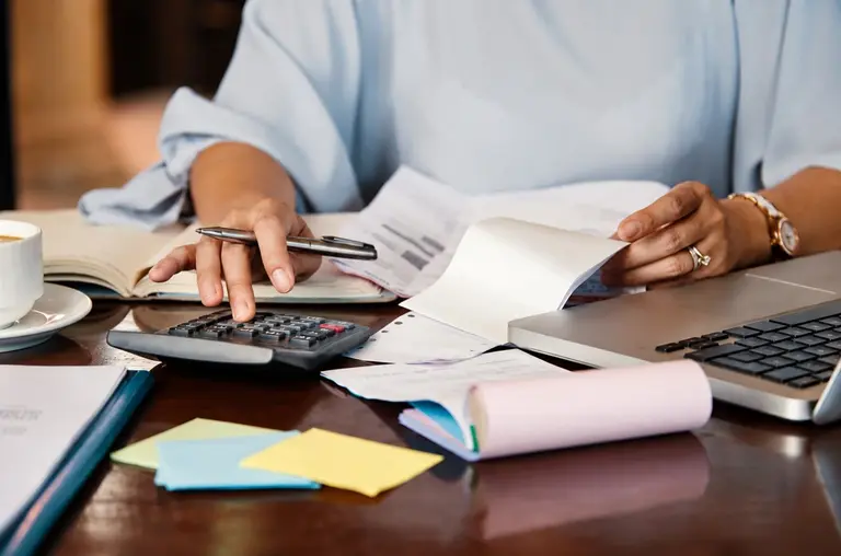 Una mujer revisa facturas y recibos, hace cuentas con una calculadora y organiza sus gastos junto a una computadora