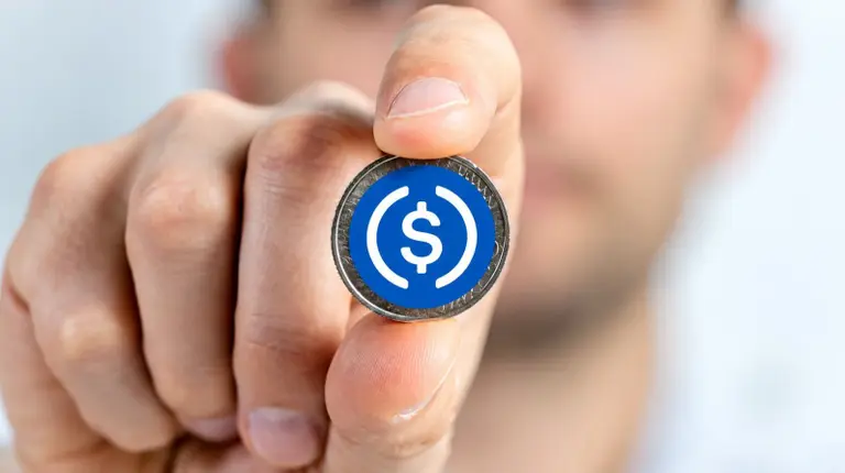 Una mano sostiene una moneda que representa una stablecoin, con un símbolo de dólar blanco sobre un fondo azul