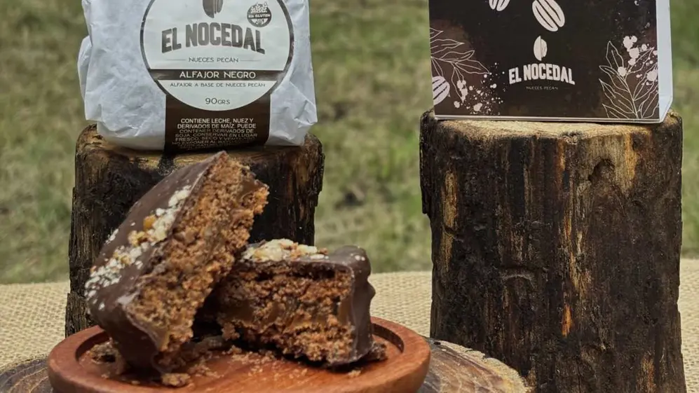 Alfajor negro El Nocedal partido al medio sobre madera, junto a su envoltorio y caja artesanal