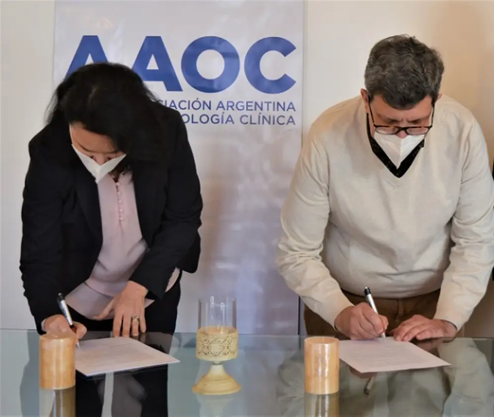 Monique Clúa (Novartis) y Dr. Bella (AAOC) firmando acuerdo