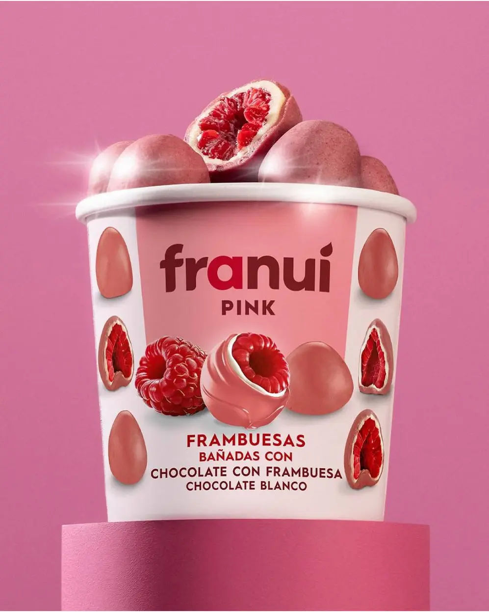 Un pote de frambuesas bañadas en chocoelate blanco sobre un fondo rosa
