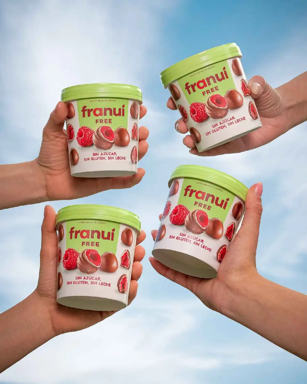 4 manos agarrando potes de Franui free, sin azucar, sin azúcar y sin leche, sobre un fondo celeste