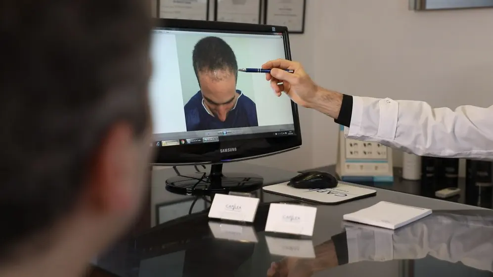 Médico de Capilea mostrando a un paciente cómo es el tratamiento en la pantalla de una computadora