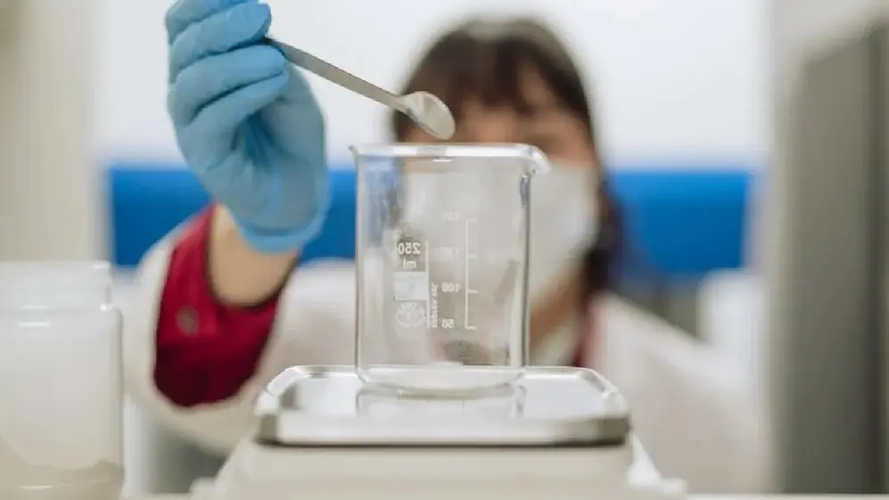Manos con guantes de laboratorio colocando producto en un frasco.