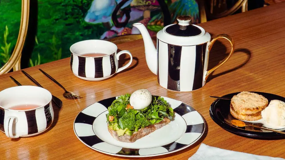 Tetera, tasas con te y platos con opciones dulces y saladas sobre una mesa de madera