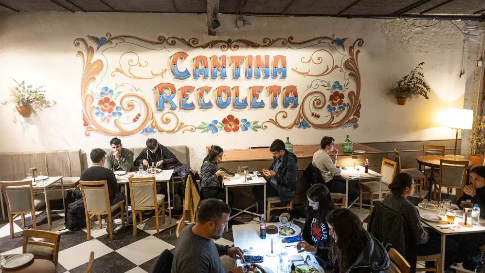 Personas sentadas en distintas sillas y mesas disfrutando en el local de Cantina Recoleta