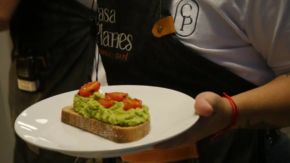 Persona con delantal llevando un plato con un plan tostado con guacamole y tomates cherries