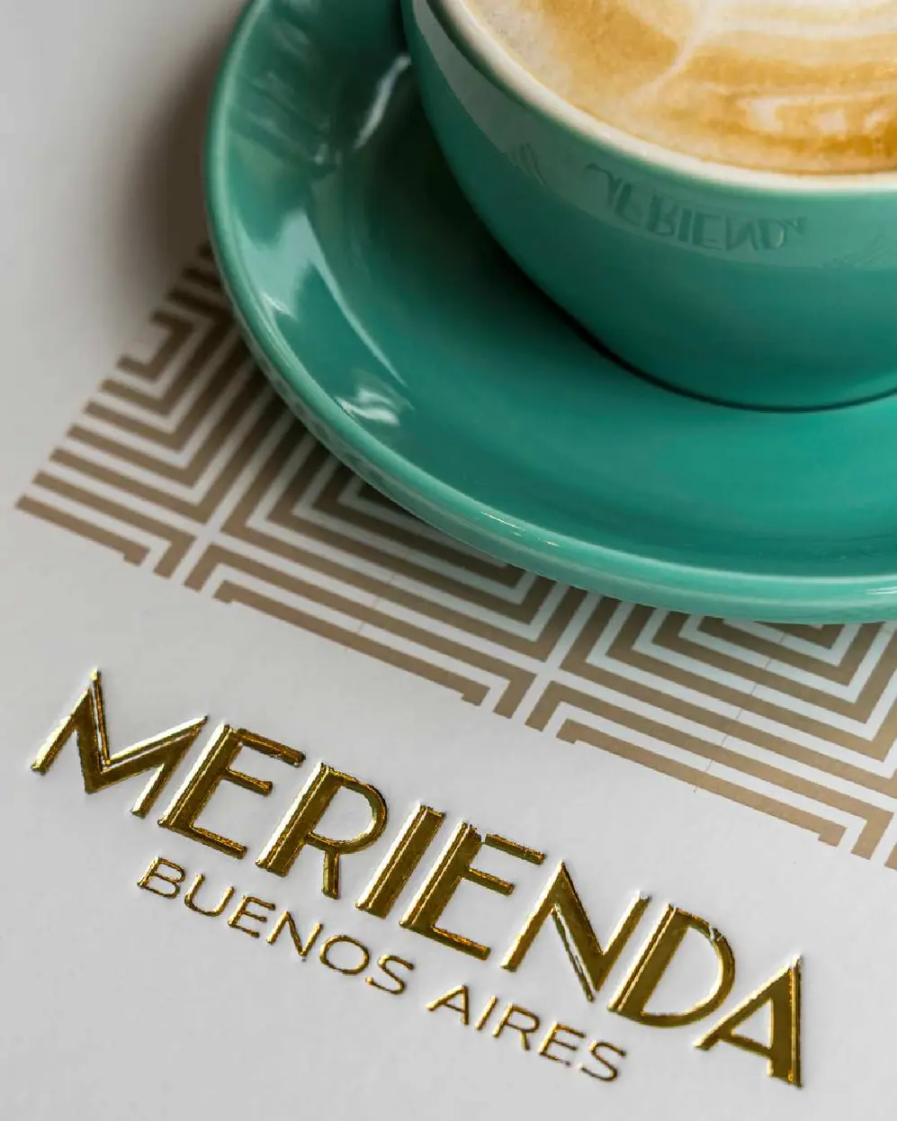 Tasa verde de cafeacute; con su plato a tono sobre un mantel que lleva el nombre del local Merienda