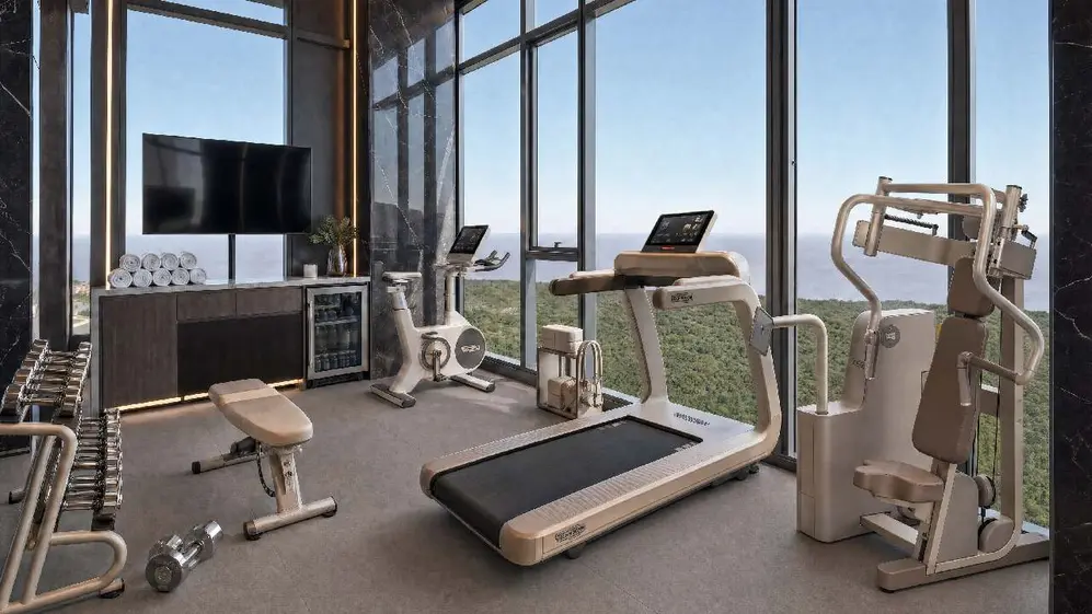 Gimnasio del edificio con distintas máquinas en piso en altura y vistas al exterior