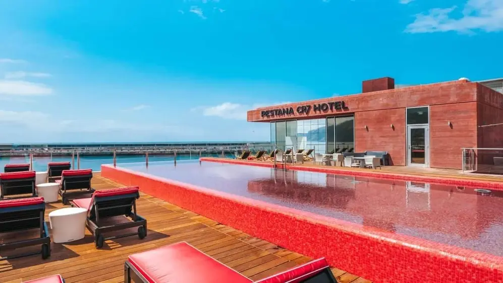Hotel con piscina roja, suelo de madera, reposeras rojas con mesas blancas