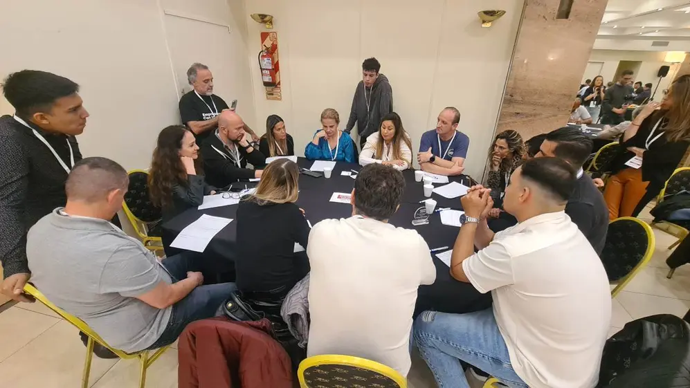 Un grupo de mujeres y hombres sentados y parados alrededor de una mesa conversando