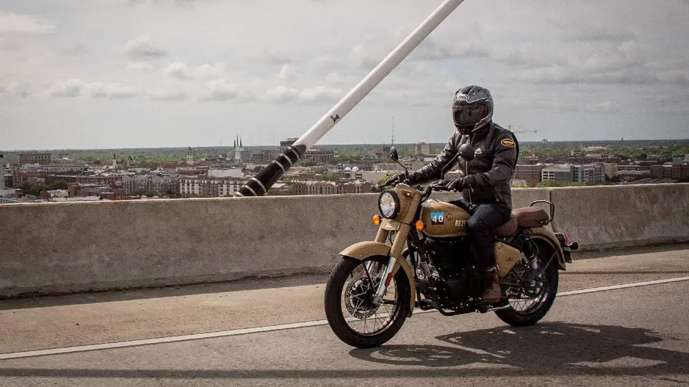 Un hombre vestido de negro paseando por una ruta en una moto color beige con edificios atrás