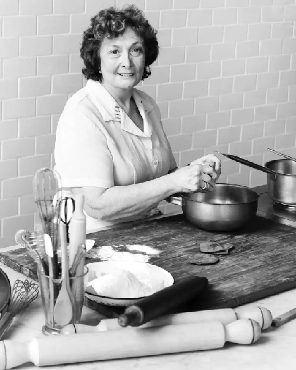 Una señora mayor cocinando con distintos elementos sobre una mesada