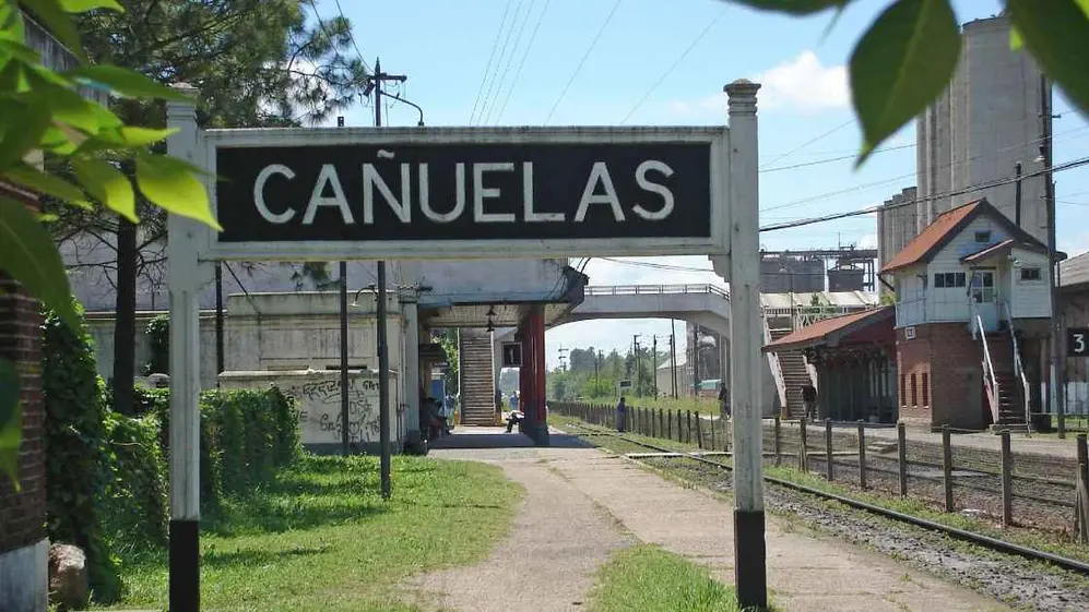 Cartel de la estación Cañuelas junto a las vías y andenes del ferrocarril.