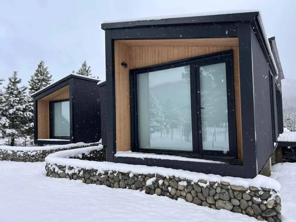Casas modulares negras con detalles en madera y grandes ventanales sobre la nieve