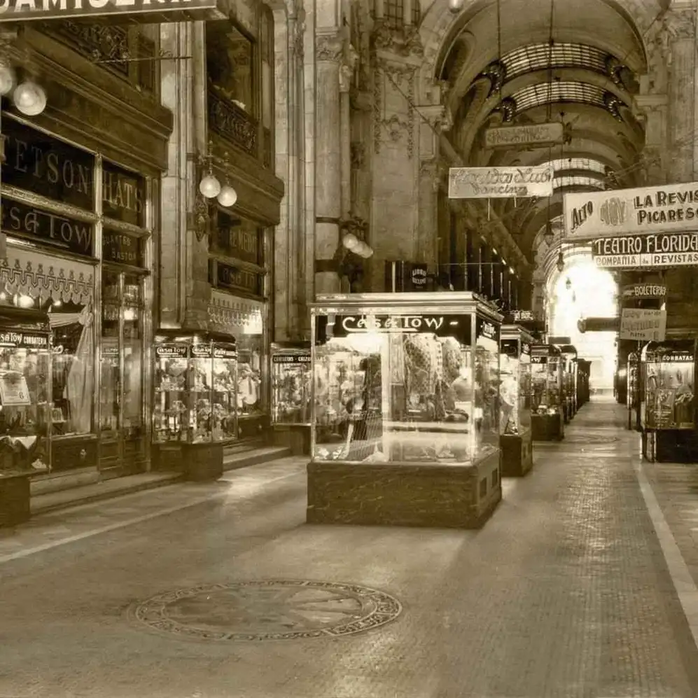 Fotografía histórica de una galería comercial con vitrinas, locales y techos abovedados.