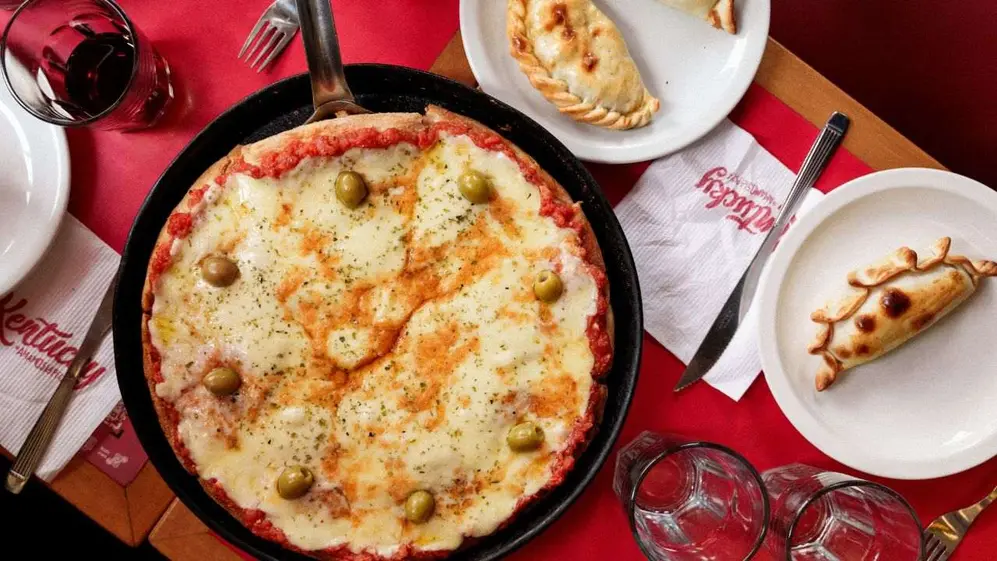 Mesa servida con pizza y empanadas de la marca (Gentileza Kentucky)