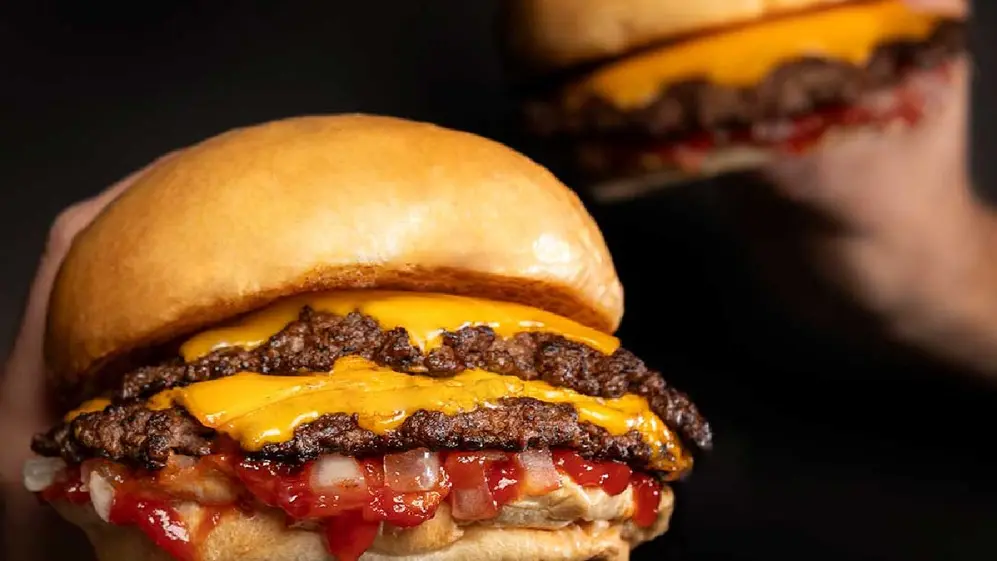 Una hamburguesa de carne doble con queso, ketchup y cebolla y otra más atrás
