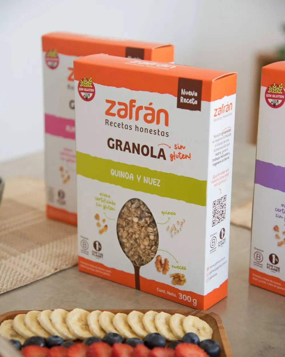 Caja de granola de la marca Zafrán con una bandeja de bananas, arándanos y frutillas adelante