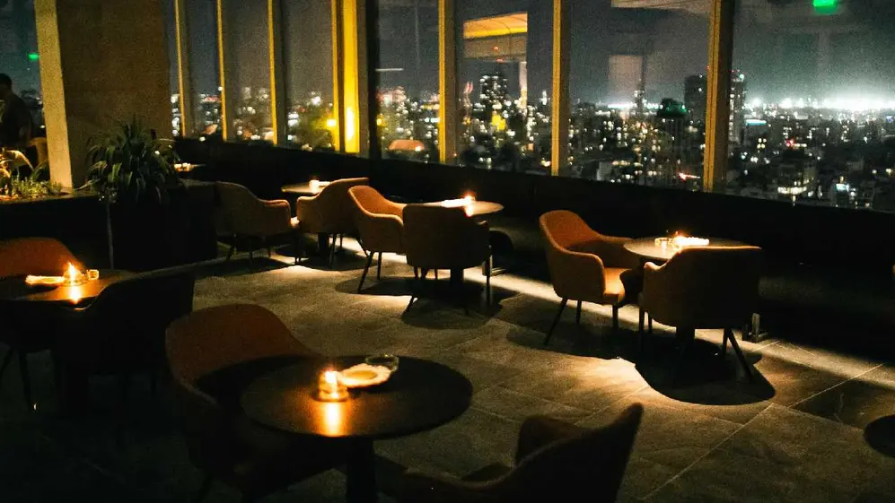Sillas y mesas con velas con ventanales atrás donde se ve la ciudad de buenos aires de noche