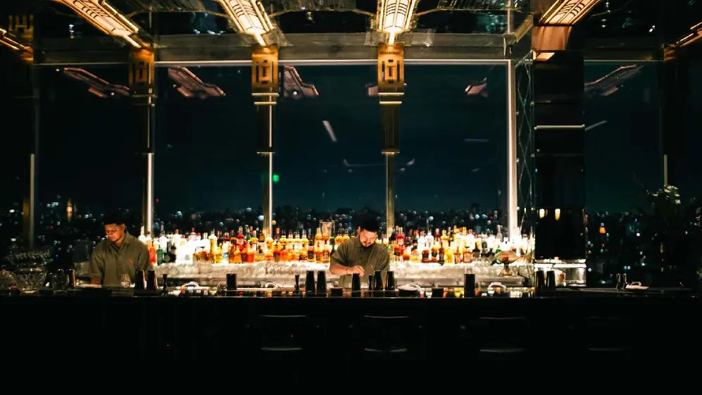 Dos bartenders preparando tragos dentrás de una barra con la ciudad de buenos aires de noche atrás