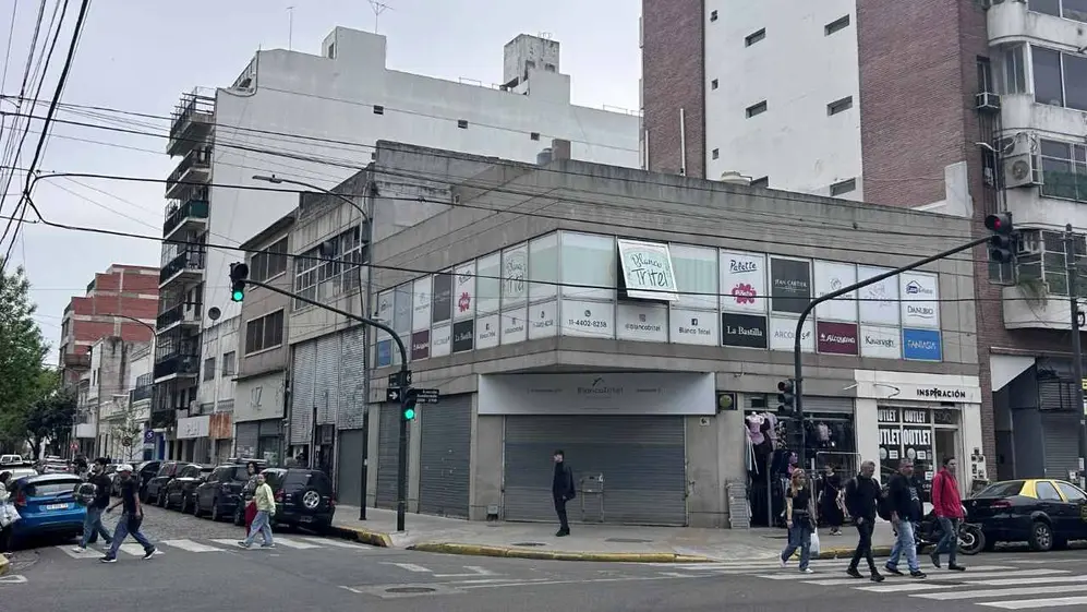 Gente cruzando una avenida con un local con sus persianas bajas de fondo