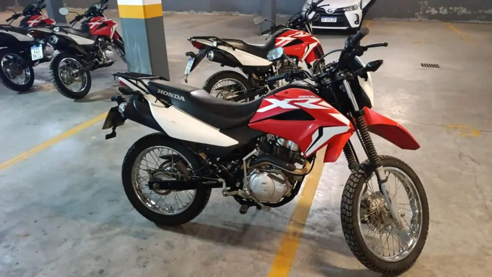 Motos Honda (de colores rojo, blanco y negro) en un estacionamiento. Al fondo hay un auto blanco