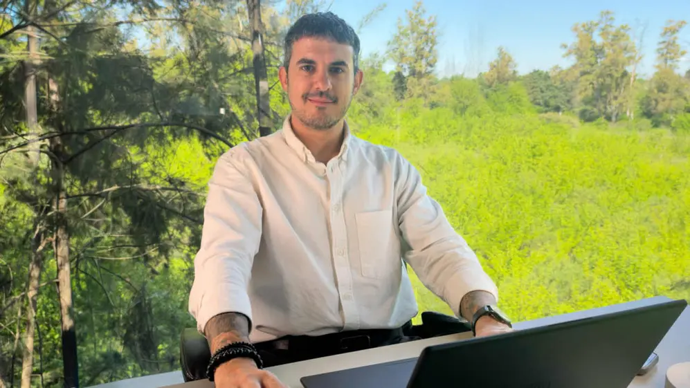 Lisandro Velazco con camisa blanca sentado con una laptop con un fondo de árboles